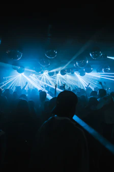 Wide shot of a packed dance floor illuminated by dynamic neon and laser lights during a night event