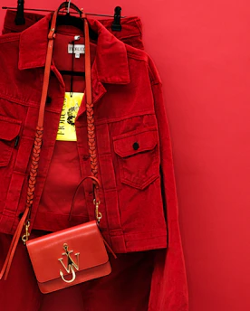A stylish red jacket hanging on a wooden hanger against a red background.