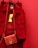 A vibrant red jacket is hanging on a red background, accompanied by a matching red handbag with a gold emblem and braided strap. The bright yellow clothing tag is prominently displayed.