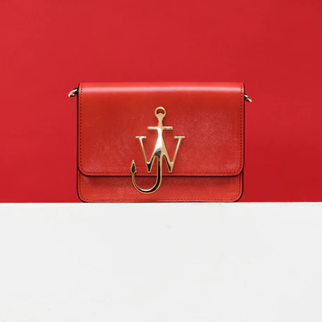 A vibrant red crossbody bag hanging on a rustic wooden hook.