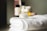 A small jar of regenerating collagen moisturizer is placed on a neatly folded, white towel. In the background, there are several blurred skincare bottles in various shapes and sizes.