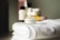 A small jar of regenerating collagen moisturizer is placed on a neatly folded, white towel. In the background, there are several blurred skincare bottles in various shapes and sizes.