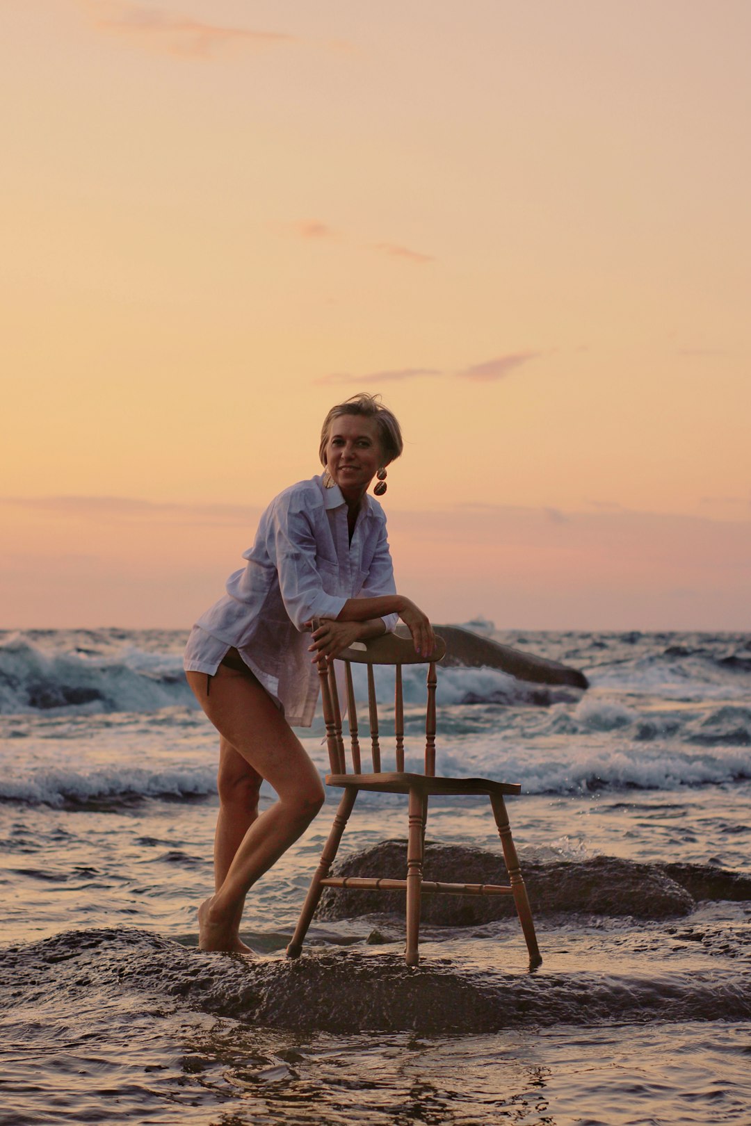 woman in white button up shirt sitting on brown wooden chair on beach during daytime