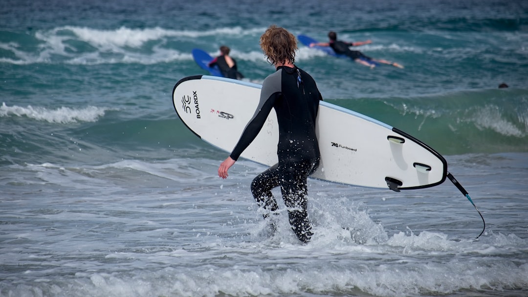 woman in black wetsuit holding white surfboard on water during daytime
