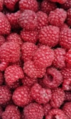 A close-up view of numerous ripe raspberries clustered together, with a rich red color and a textured surface.