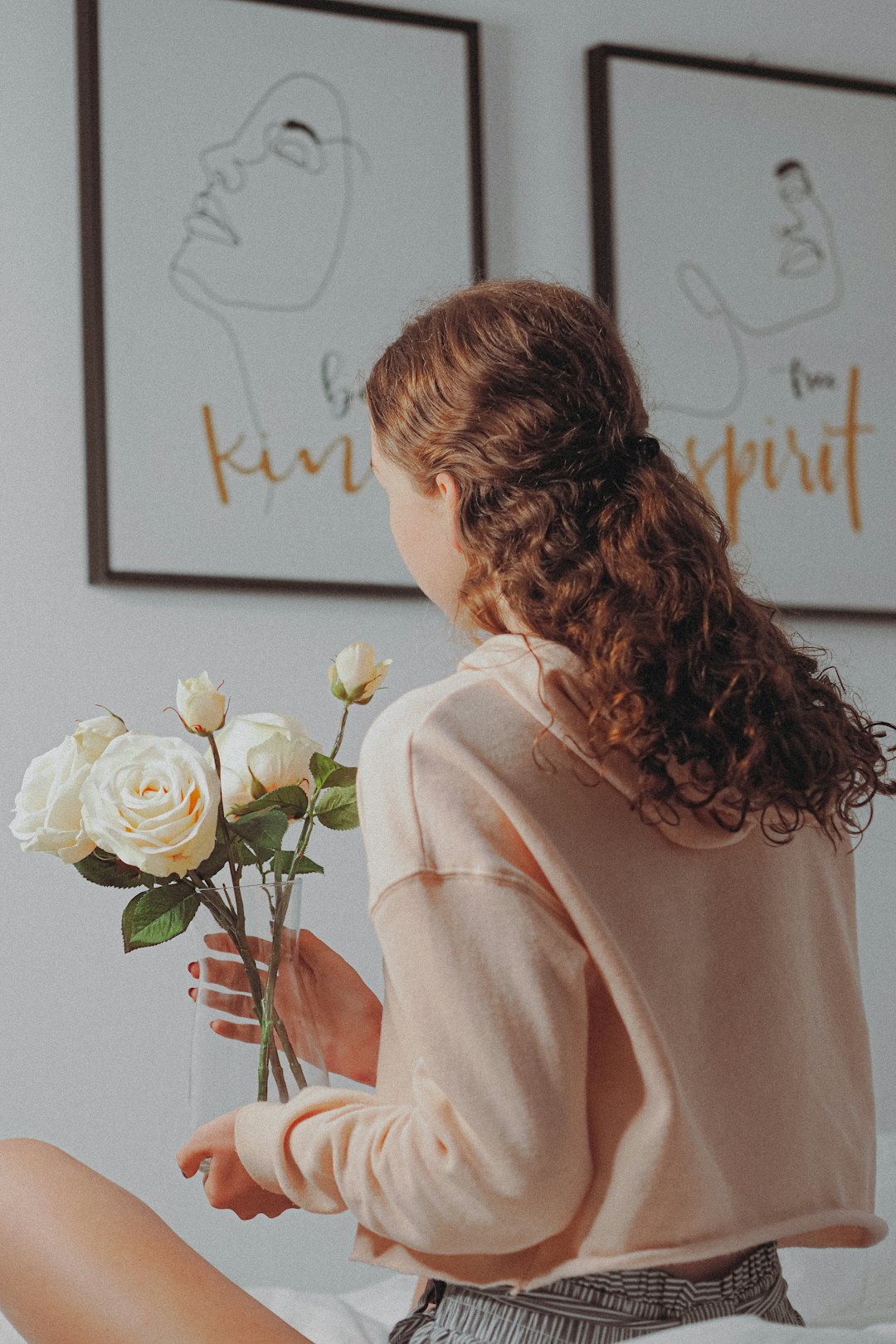 woman in pink hoodie standing in front of white roses