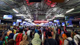 Wide shot of a crowded railway station with multiple LED advertising screens visible.