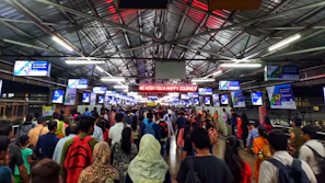 Wide shot of a crowded railway station with multiple LED advertising screens visible.
