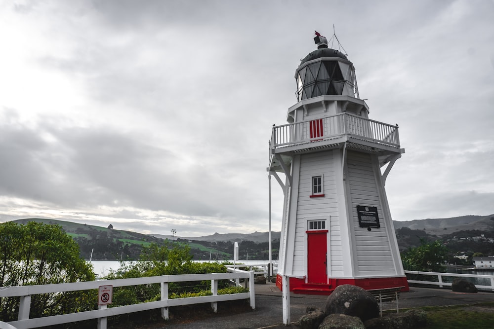 farol de concreto branco e vermelho sob céu nublado durante o dia