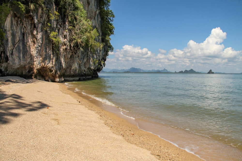 brown sand beach near green and brown rock formation under blue sky during daytime