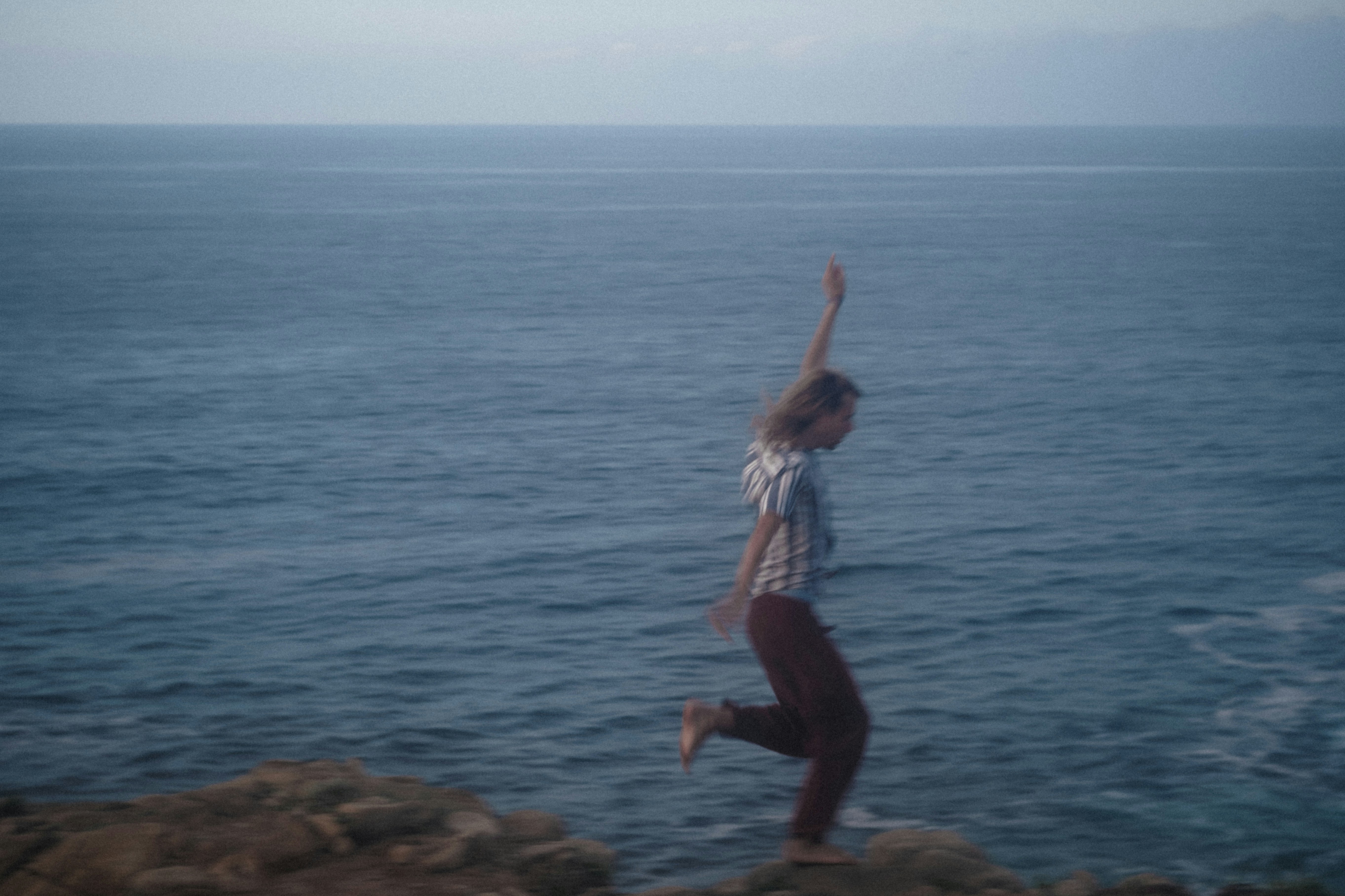 woman in white tank top and black pants standing on brown rock near body of water