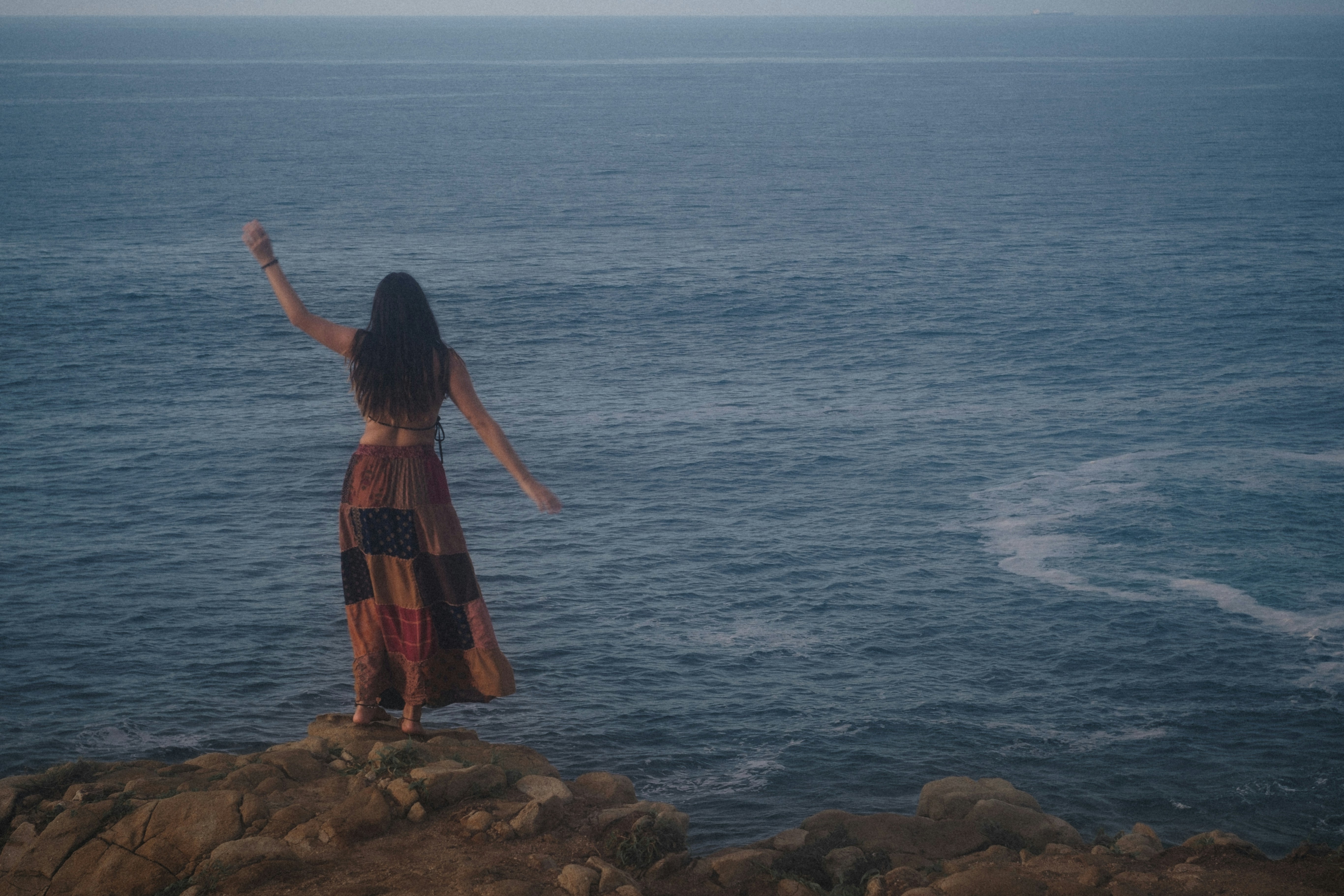 young hippie girl dancing in front of the wide blue pazific ocean
