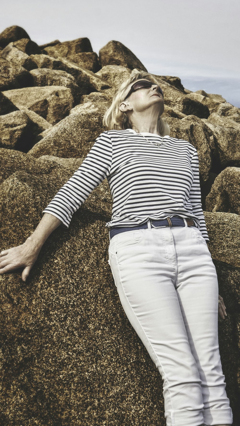 woman in black and white striped long sleeve shirt and white pants sitting on brown rock