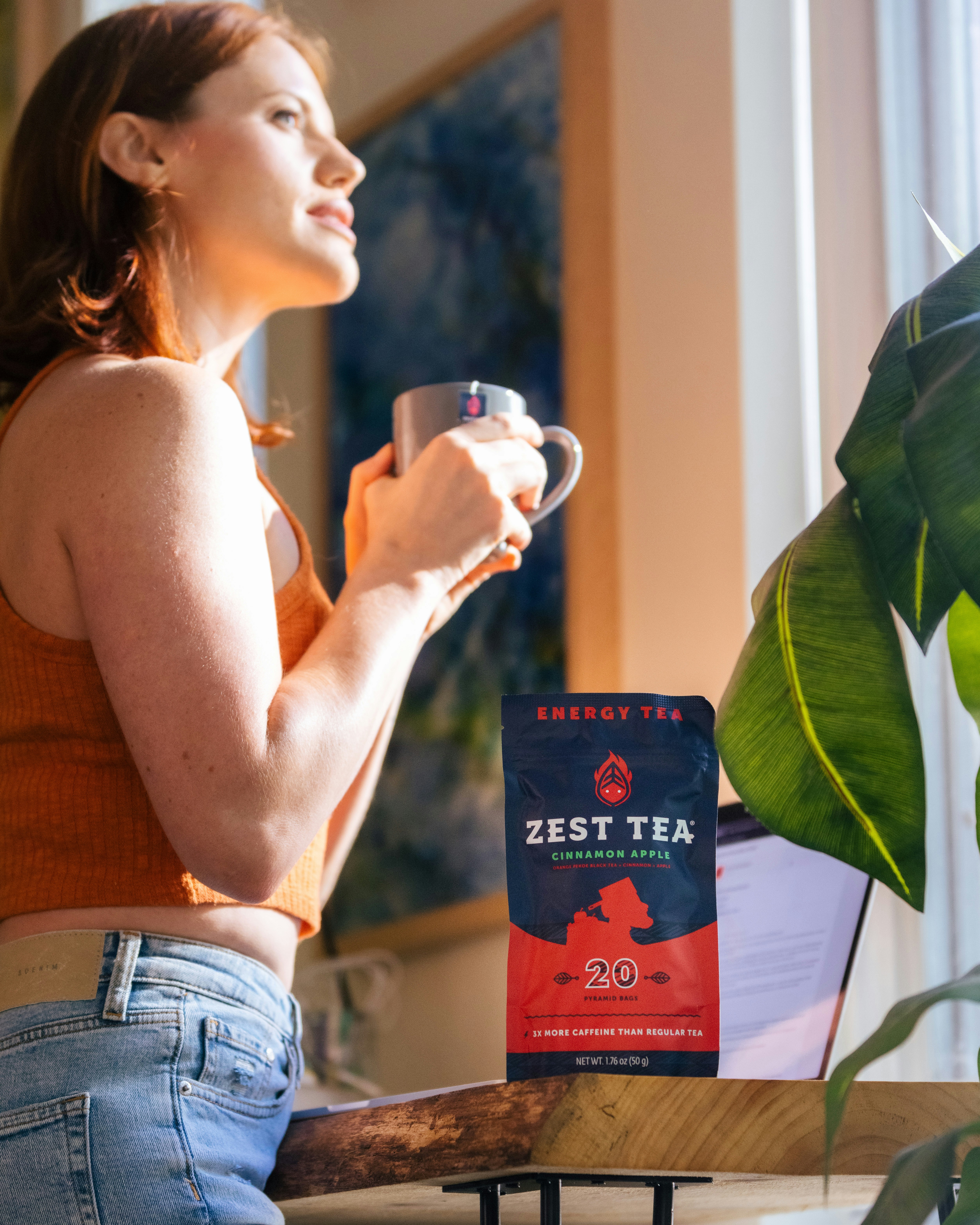 woman in brown tank top and blue denim jeans holding white ceramic mug