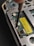 A close-up view of the inside of an electronic device, possibly a smartphone or a handheld gadget. The image focuses on a circuit board with small components, wires, and a yellow barcode sticker. A screwdriver is visible engaging with a screw, suggesting a repair or assembly process.