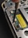 A close-up view of the inside of an electronic device, possibly a smartphone or a handheld gadget. The image focuses on a circuit board with small components, wires, and a yellow barcode sticker. A screwdriver is visible engaging with a screw, suggesting a repair or assembly process.