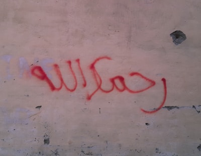 Red spray-painted Arabic script is visible on a textured wall with chipped paint and uneven surface.