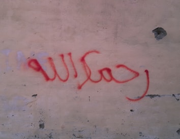 Red spray-painted Arabic script is visible on a textured wall with chipped paint and uneven surface.