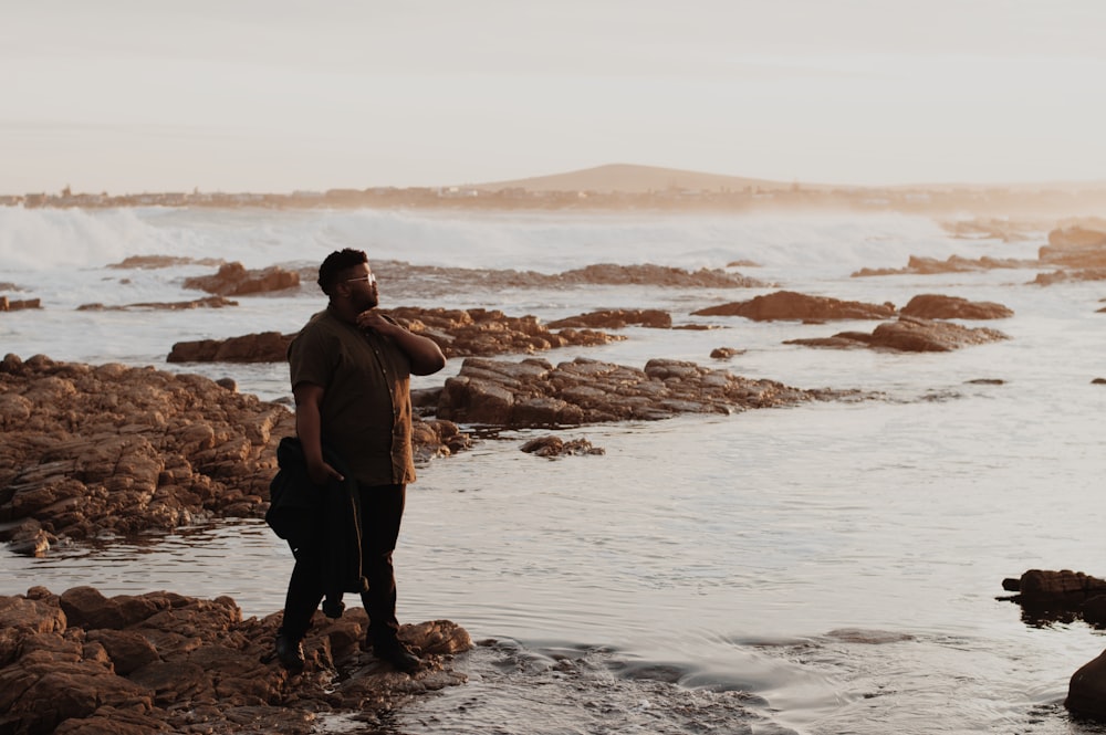 man in black shorts standing on brown rock near body of water during daytime