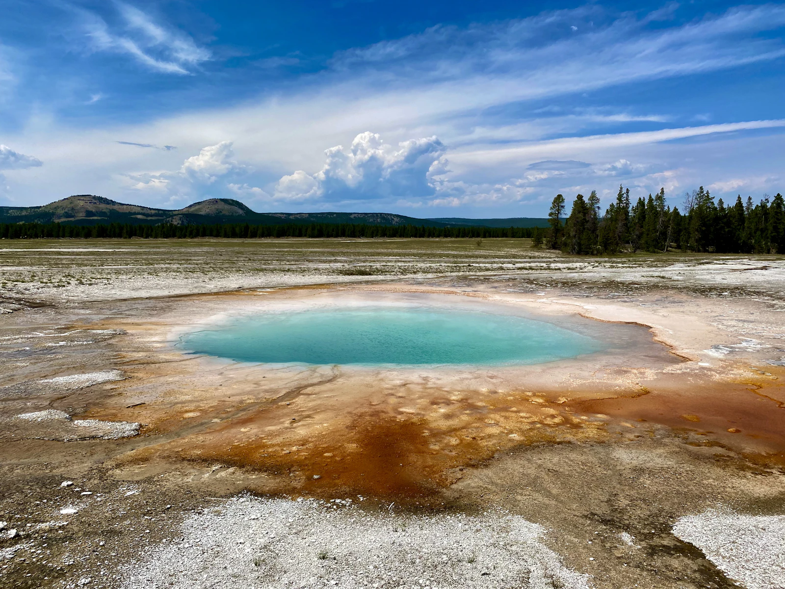 A hot spring ringed with orange bacterial mats in a Yellowstone geyser basin