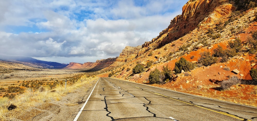 gray concrete road between brown mountains under white clouds and blue sky during daytime