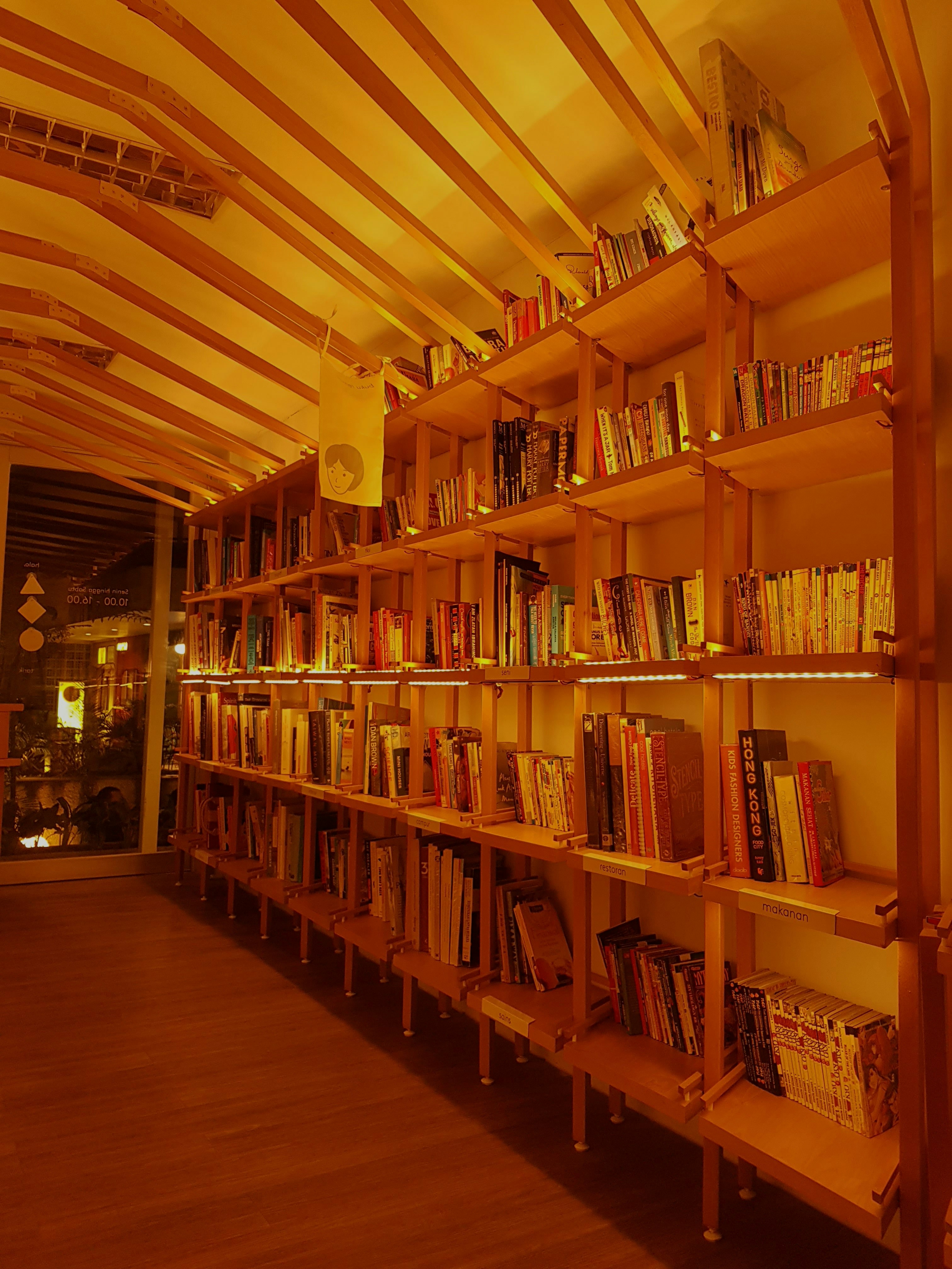 Neatly stacked colorful books on wooden shelf, warm reading nook lighting