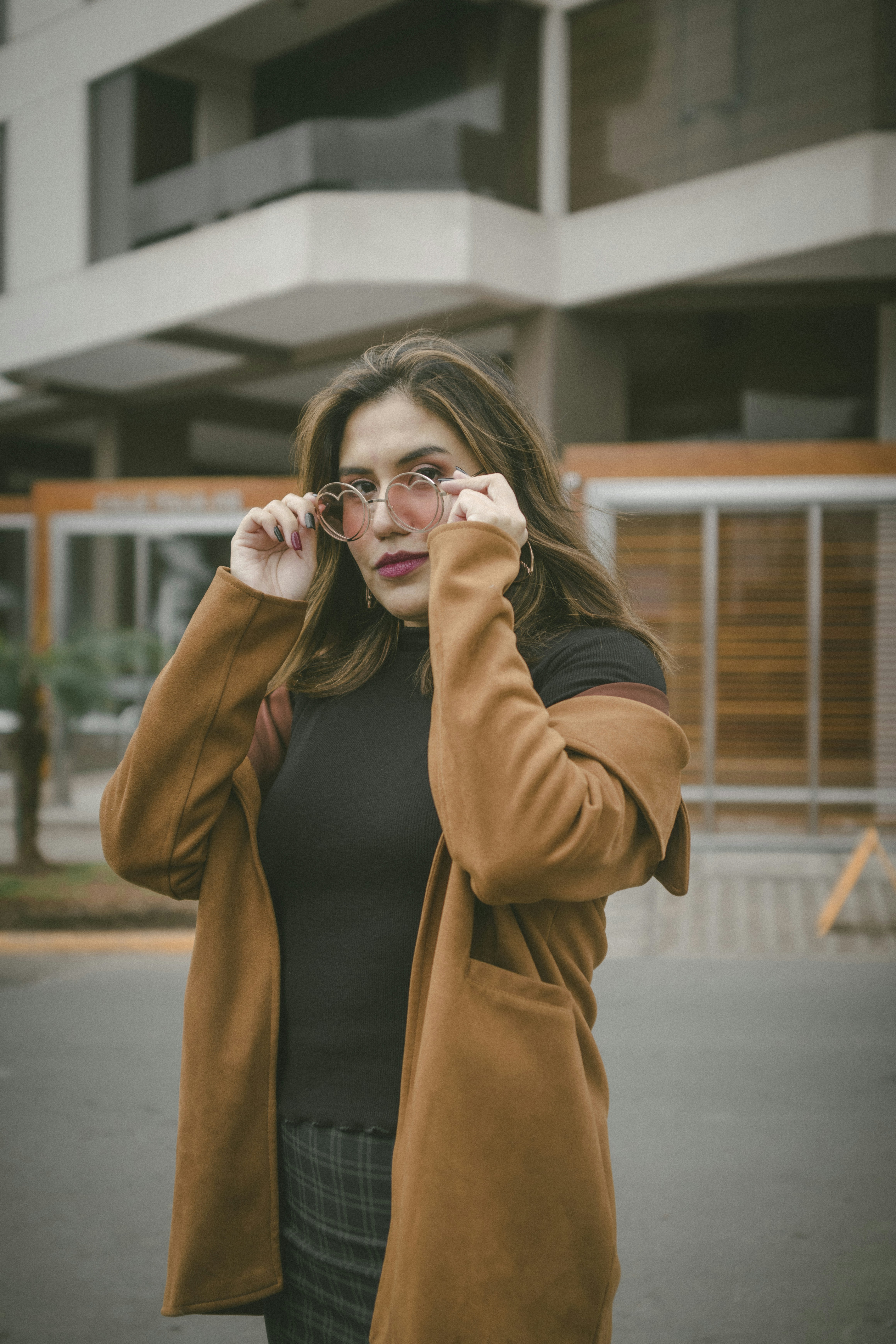 woman in brown coat holding her eyeglasses