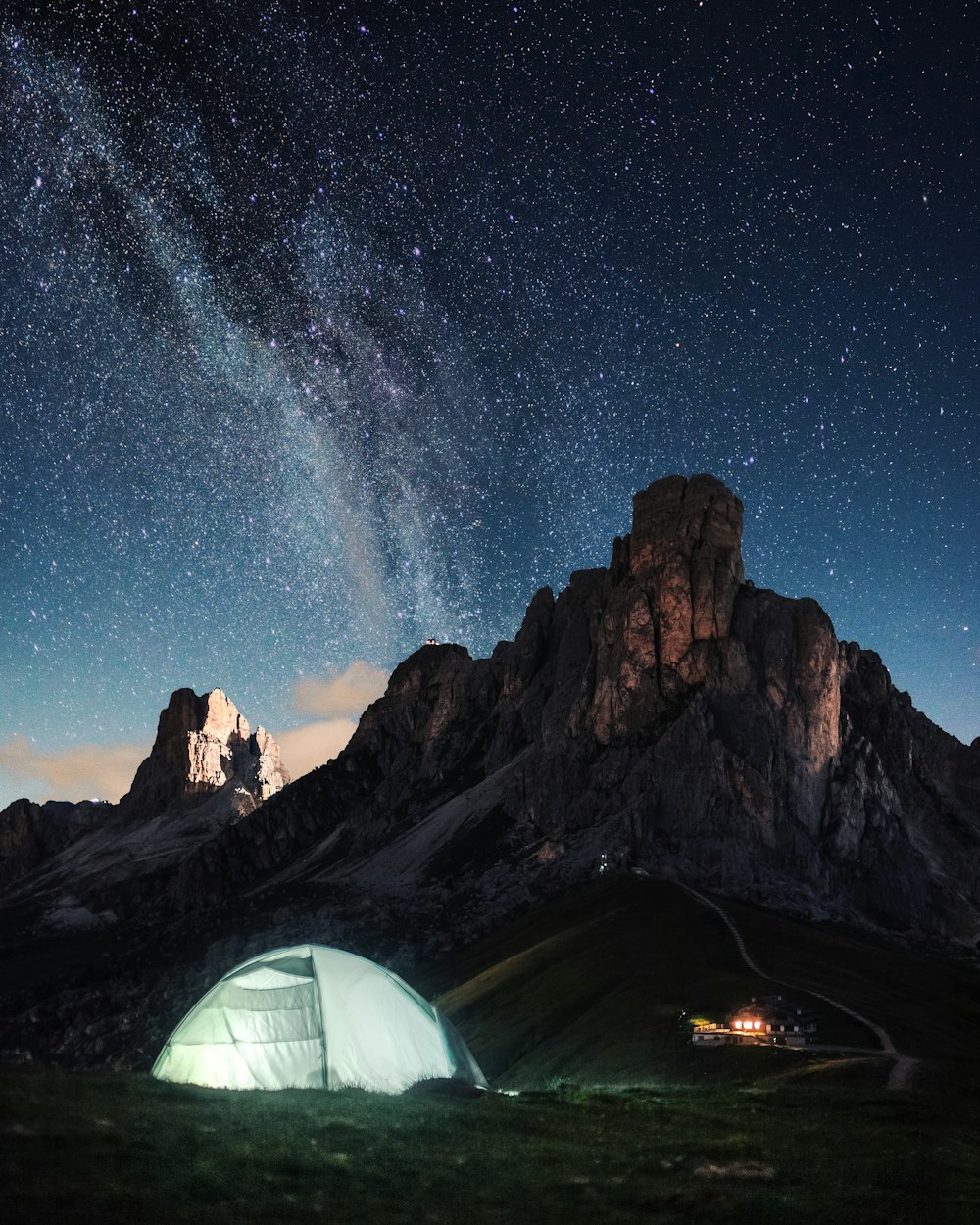 夜間の青空の下、茶色の岩層近くの白いドームテント