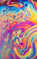 Vibrant, swirling patterns of vivid colors create an abstract and psychedelic effect. The image displays a fluid, marbled design with intricate curves and waves, resembling a kaleidoscope of hues blending seamlessly.