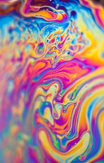 Vibrant, swirling patterns of vivid colors create an abstract and psychedelic effect. The image displays a fluid, marbled design with intricate curves and waves, resembling a kaleidoscope of hues blending seamlessly.