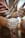 A close-up view of a person's hands, covered in chalk, gripping a climbing rope attached to a harness. The hand is secured to a carabiner, showcasing the preparation for rock climbing or a similar sport. The background is blurred, focusing on the hands and equipment.