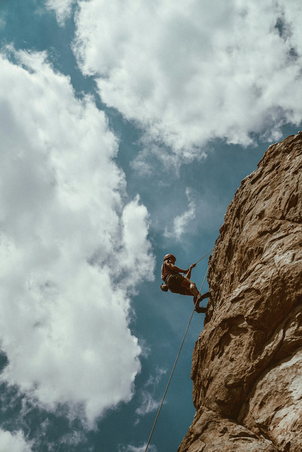 man in red jacket climbing on brown rock mountain under blue and white sunny cloudy sky