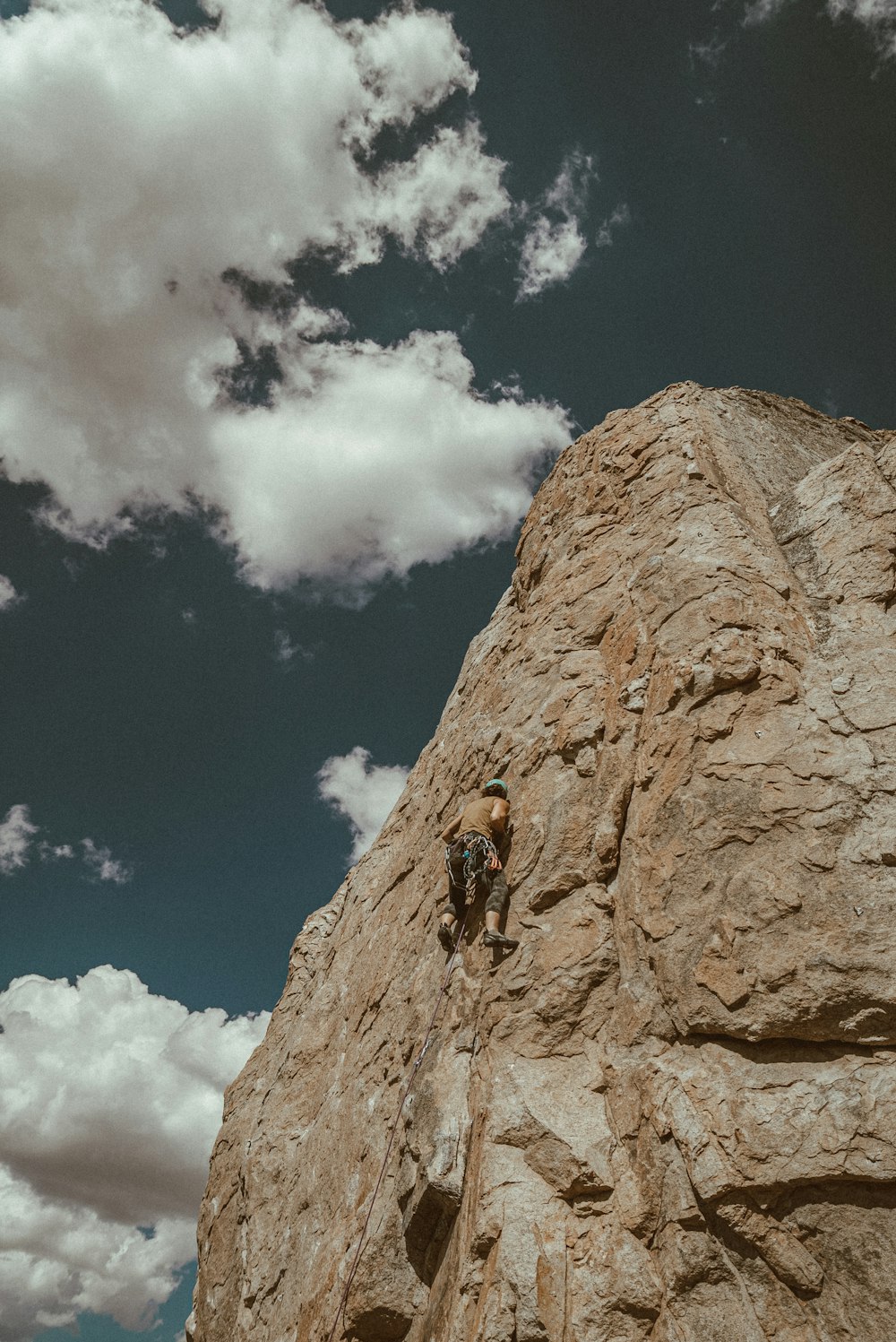 person climbing on brown rock formation under blue and white sunny cloudy sky during daytime