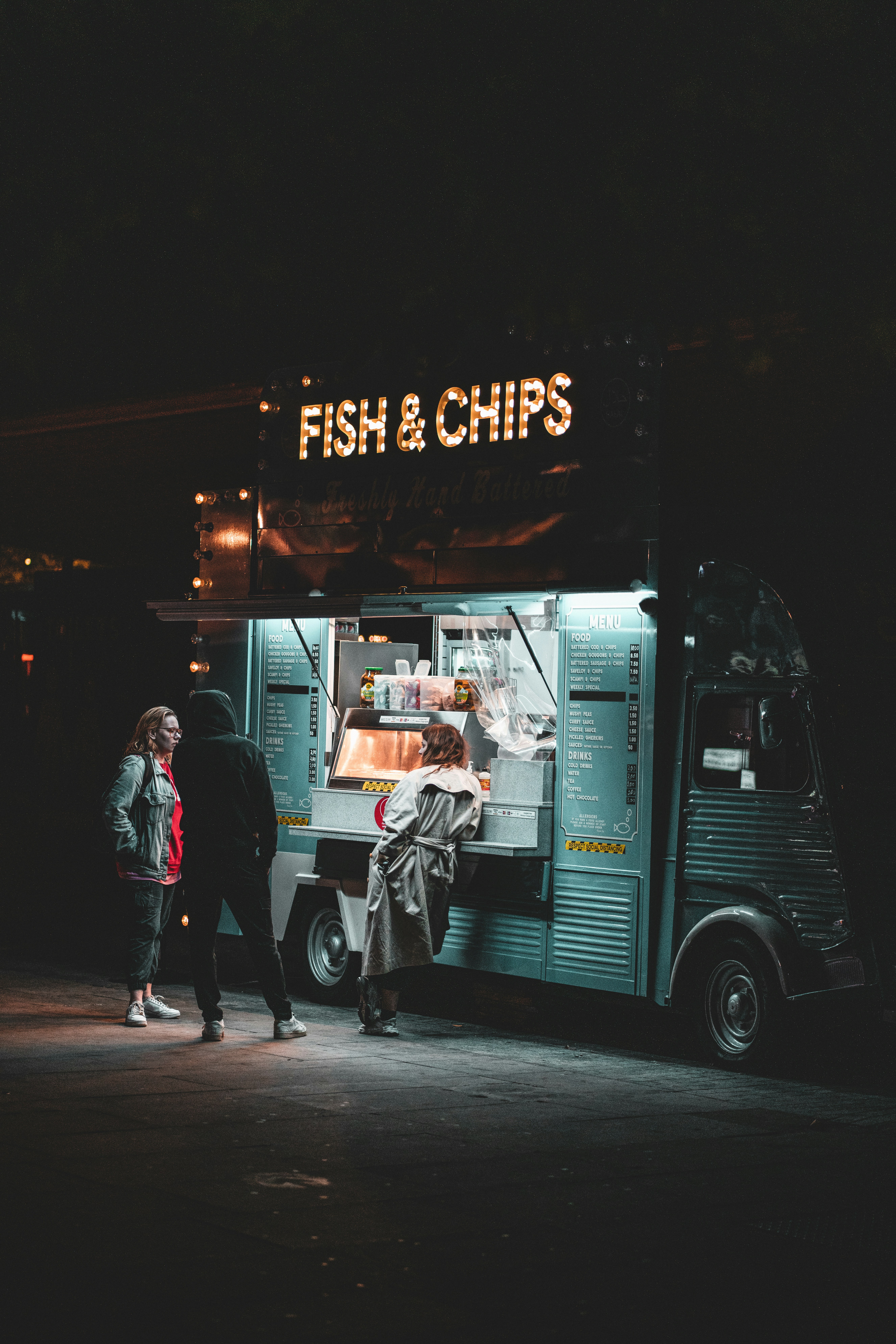 man in black jacket standing in front of white van during night time