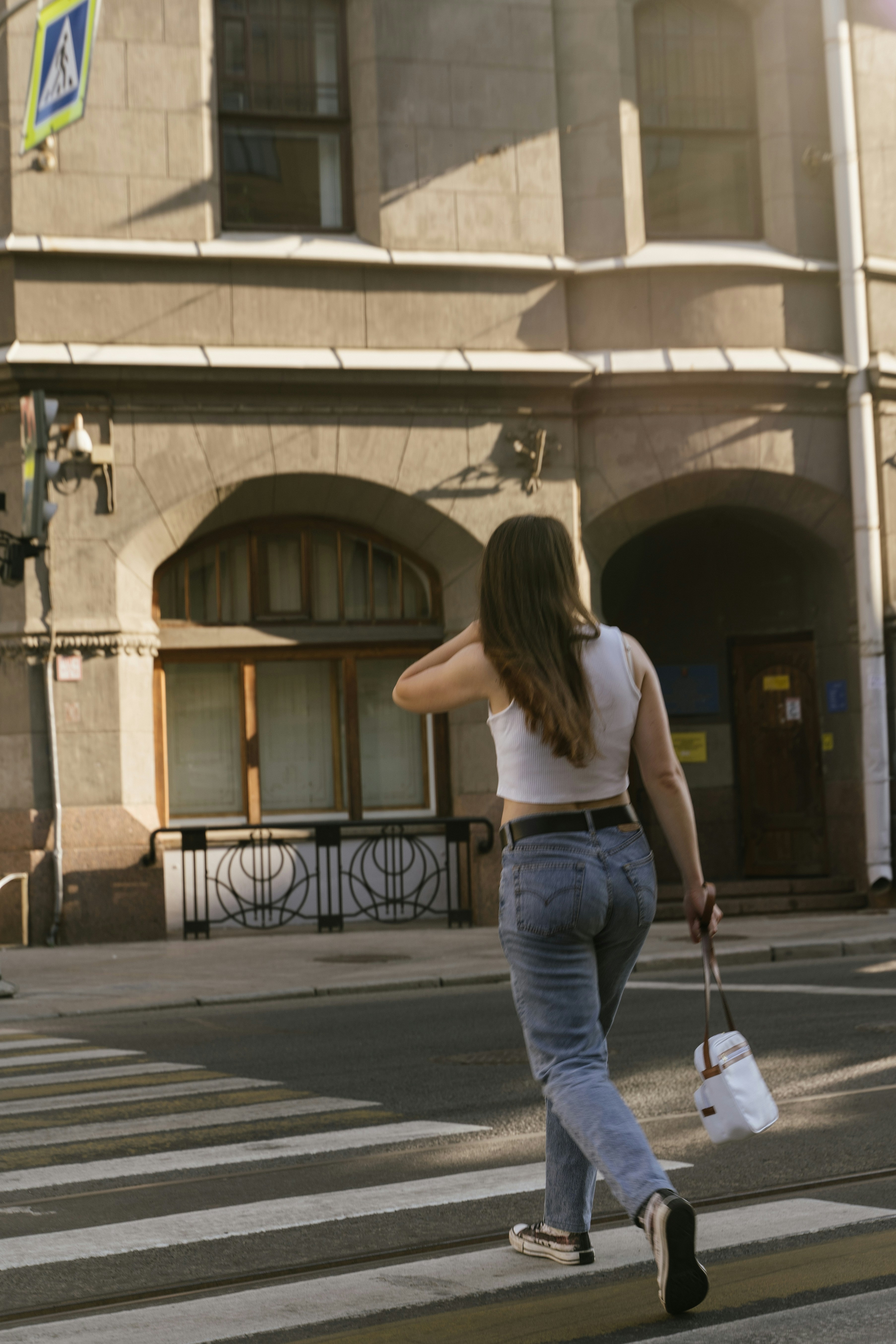 woman in white tank top and blue denim jeans walking on sidewalk during daytime