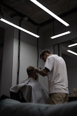 man in white shirt cutting hair of man in black and white stripe shirt