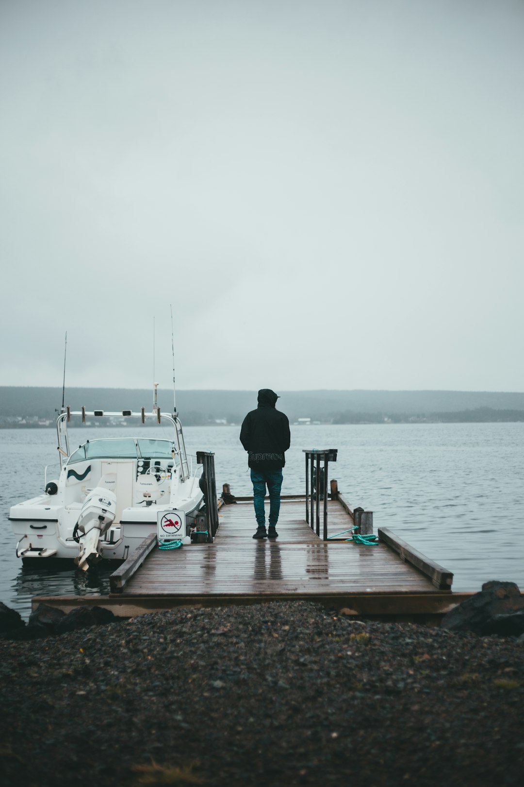 man in black jacket and pants standing on dock near white motor boat during daytime