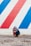 A bulldog wearing a colorful hoodie sits on a gravel surface in front of a mural with diagonal red, white, and blue stripes.