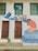 A mural painted on a building wall featuring a person in an orange shirt kneeling by a representation of water, surrounded by blue leaves and flowers. The art also depicts a blue bird in flight. Two brown wooden doors are beneath two green shuttered windows. A small potted plant is placed in front of one door.