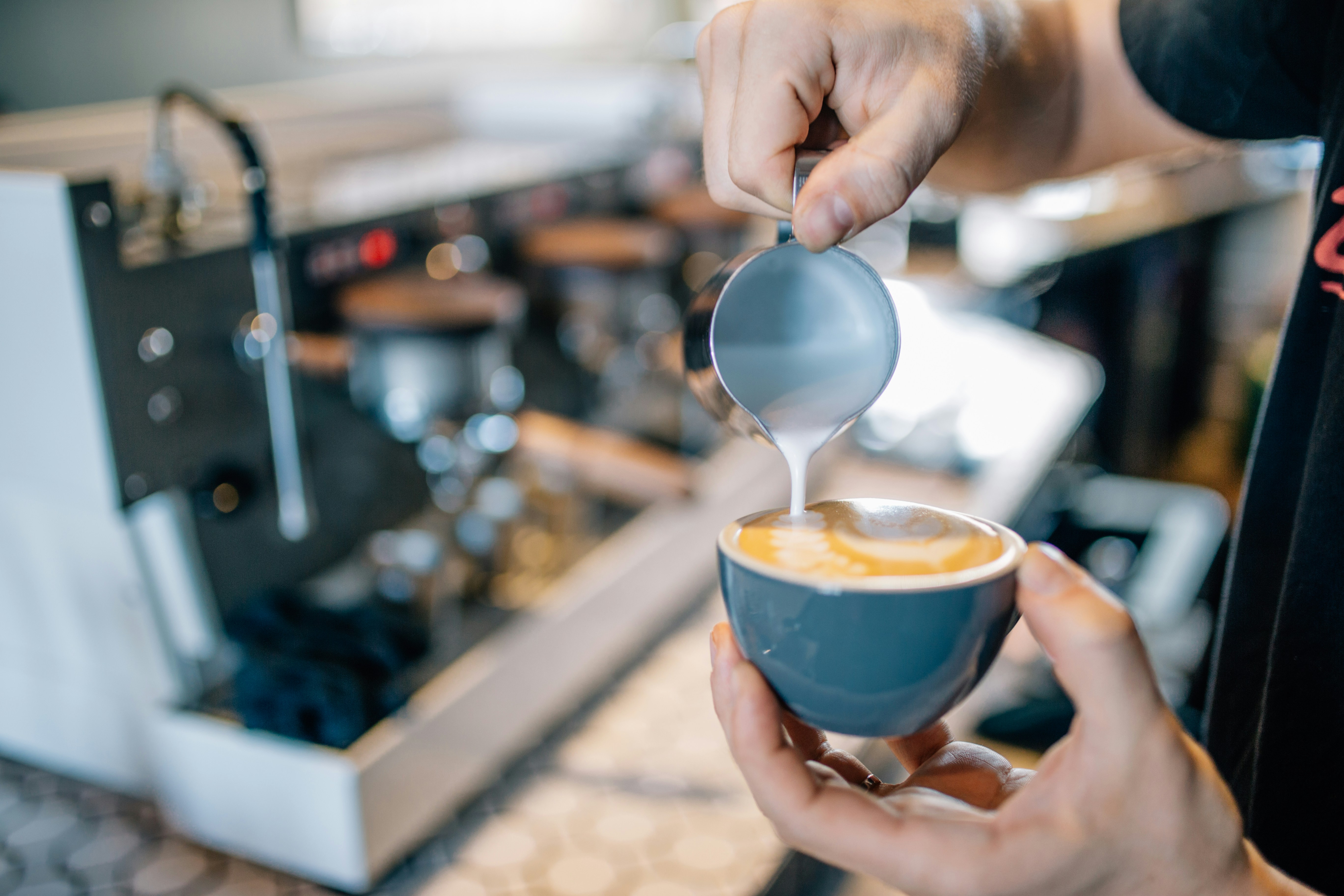Barista pouring latte art into blue ceramic bowl
