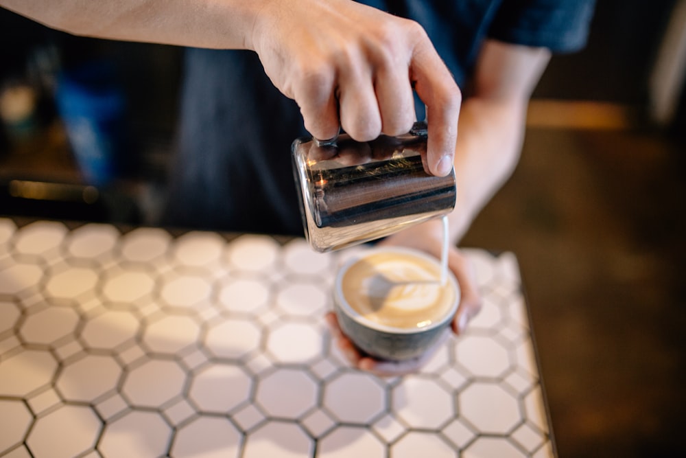 person holding black smartphone near brown and white ceramic cup with brown liquid