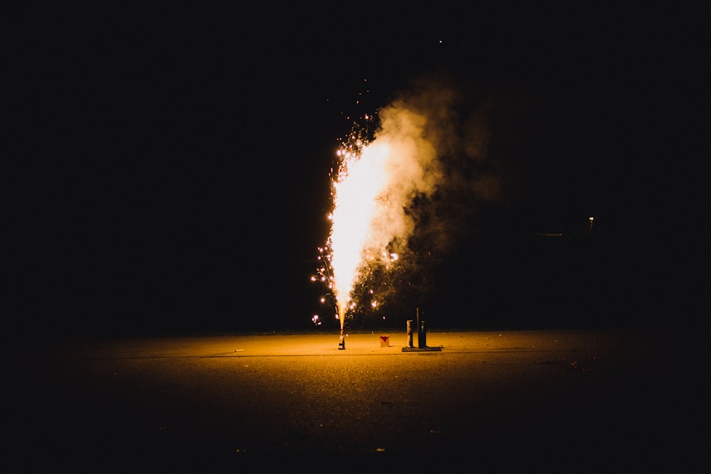 person standing on sand with fire during night time