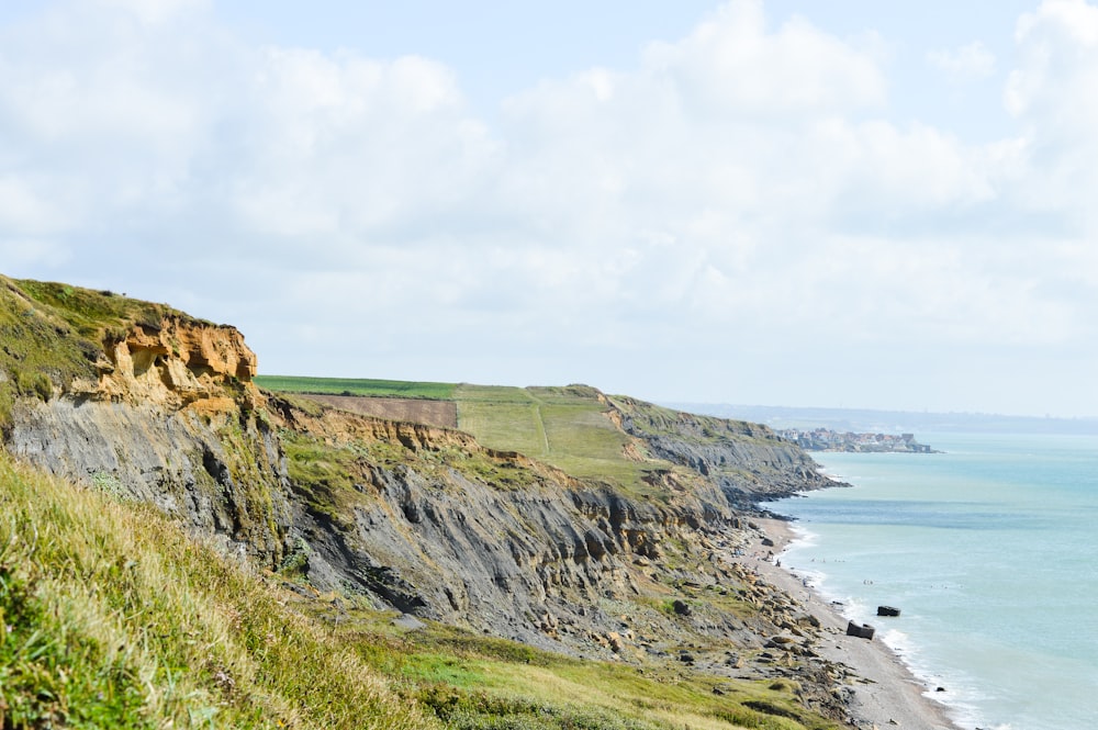 green grass field on hill near sea under white clouds during daytime