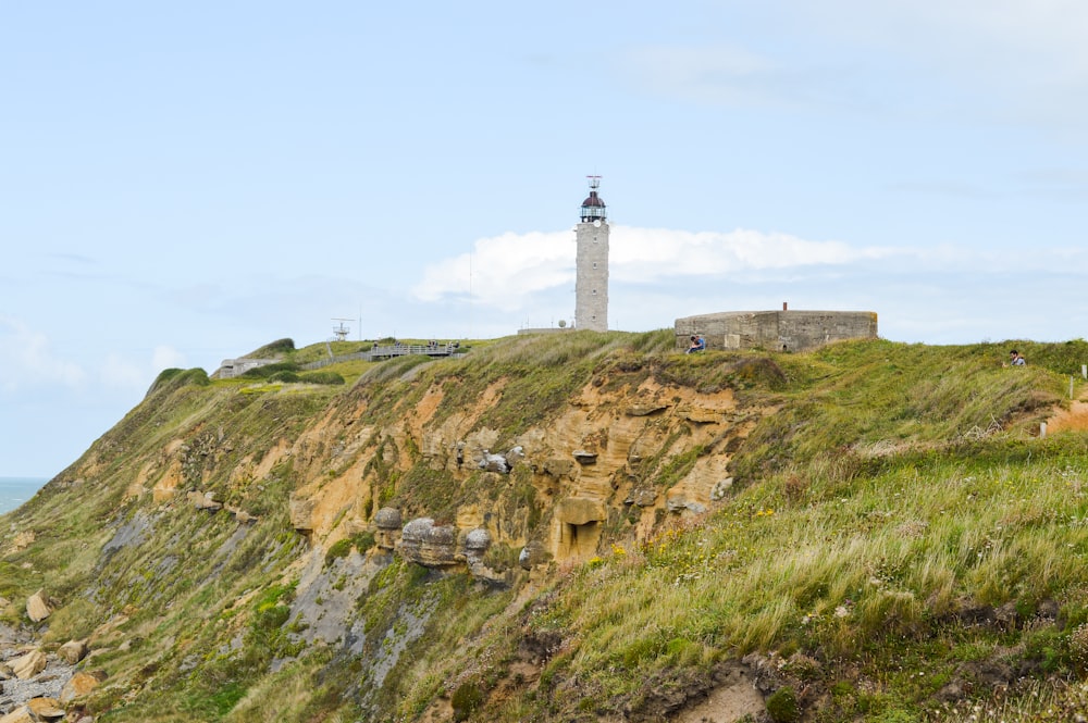 white and black lighthouse on brown and green grass field under blue sky during daytime