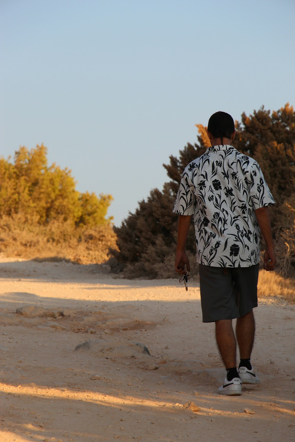 낮 동안 갈색 모래 위에 서 있는 흑백 꽃 셔츠를 입은 남자