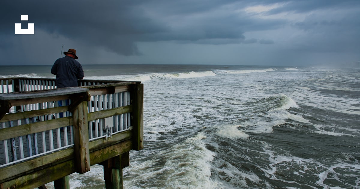 Person in black jacket sitting on brown wooden dock over sea waves