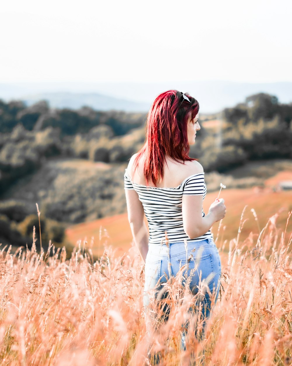 woman in white and black stripe tank top and blue denim jeans standing on brown grass