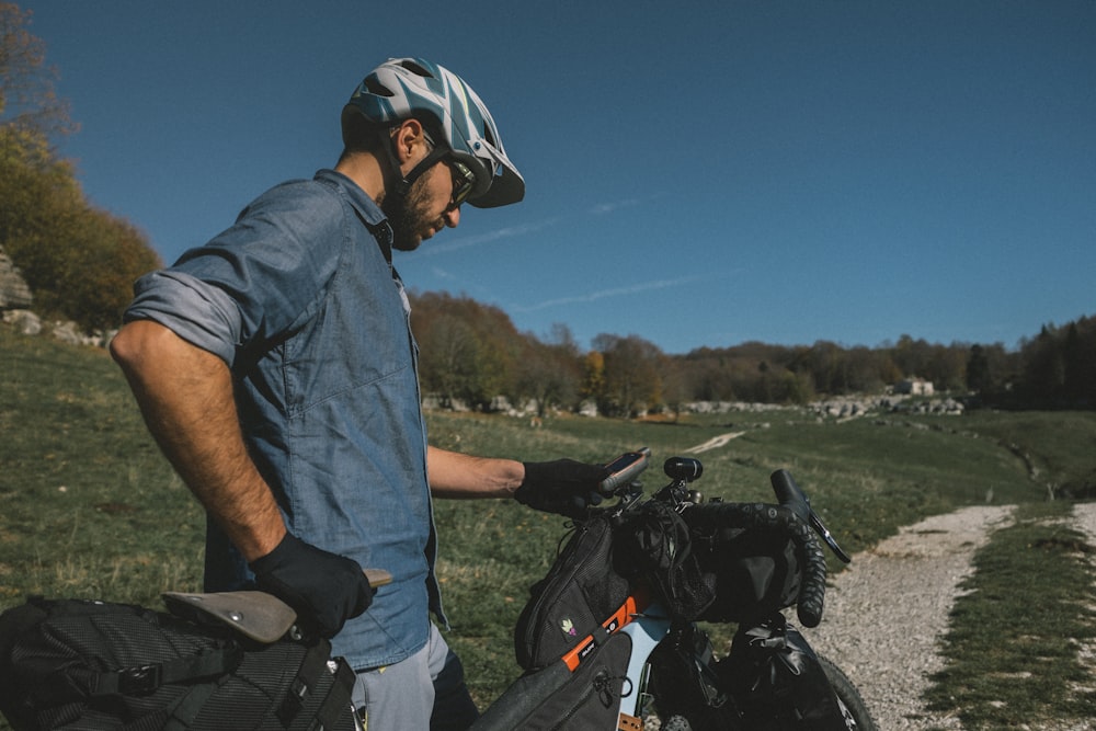 man in blue shirt and blue denim jeans standing beside black motorcycle during daytime