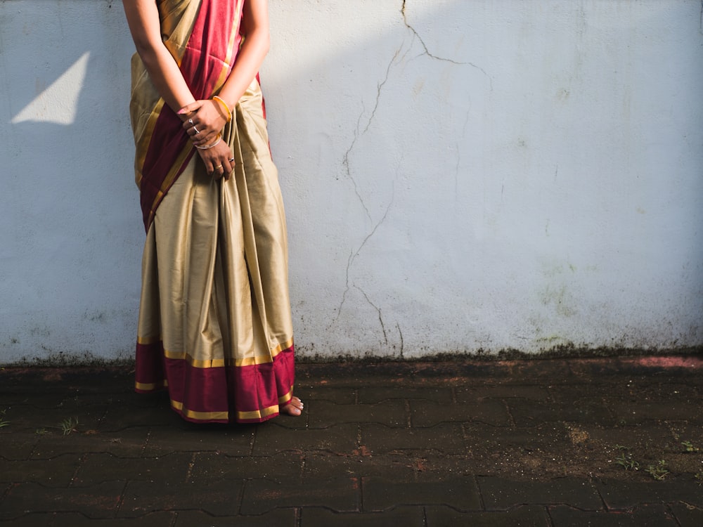 woman in red and brown sari standing beside white wall