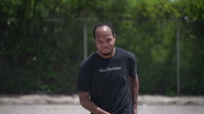 Side view of a model walking outdoors wearing a black t-shirt with a modern scripture print